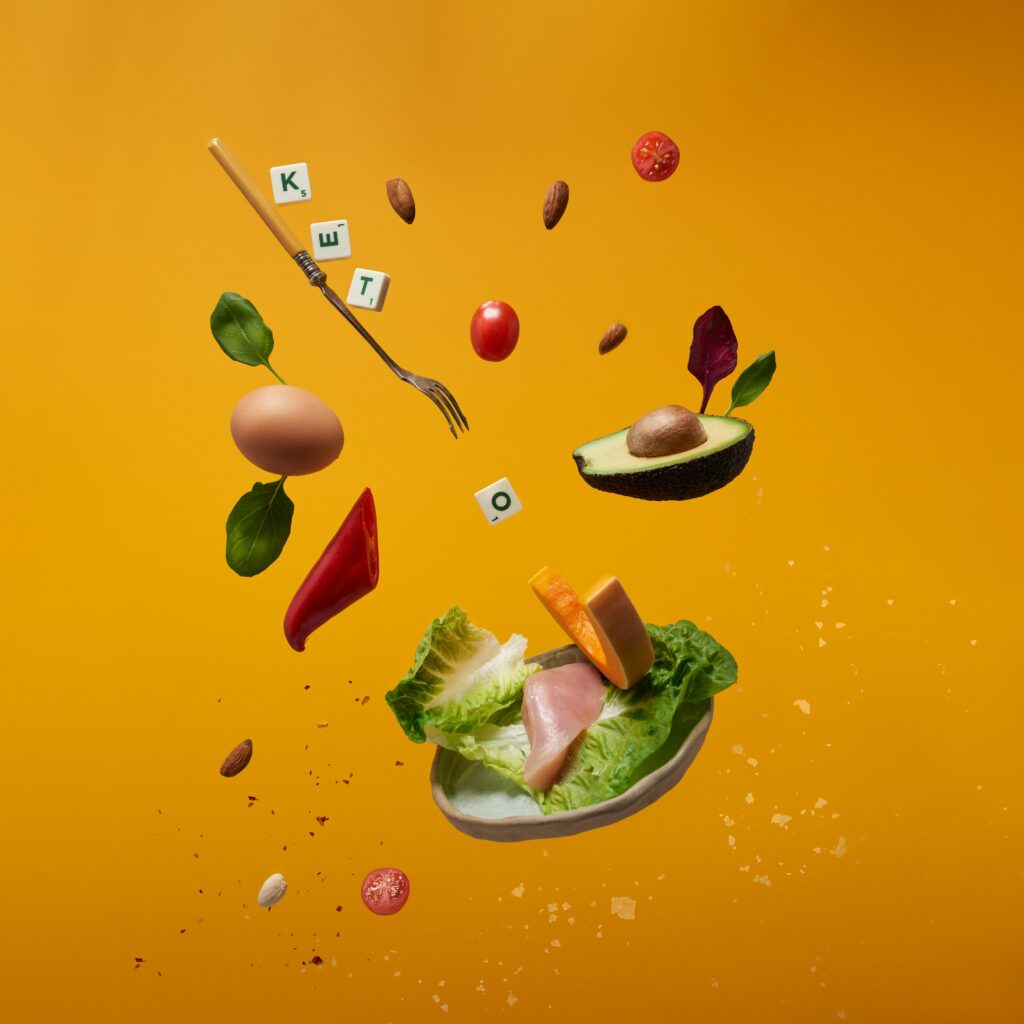 A picture of a fork, a plate falling with greens, eggs, avocado, tomatoes, almonds and the word KETO