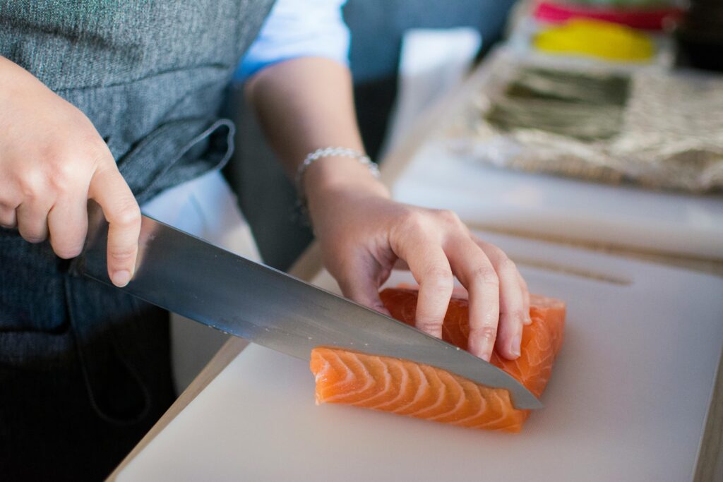 A person slicing a salmon fillet with a knife the proper way.